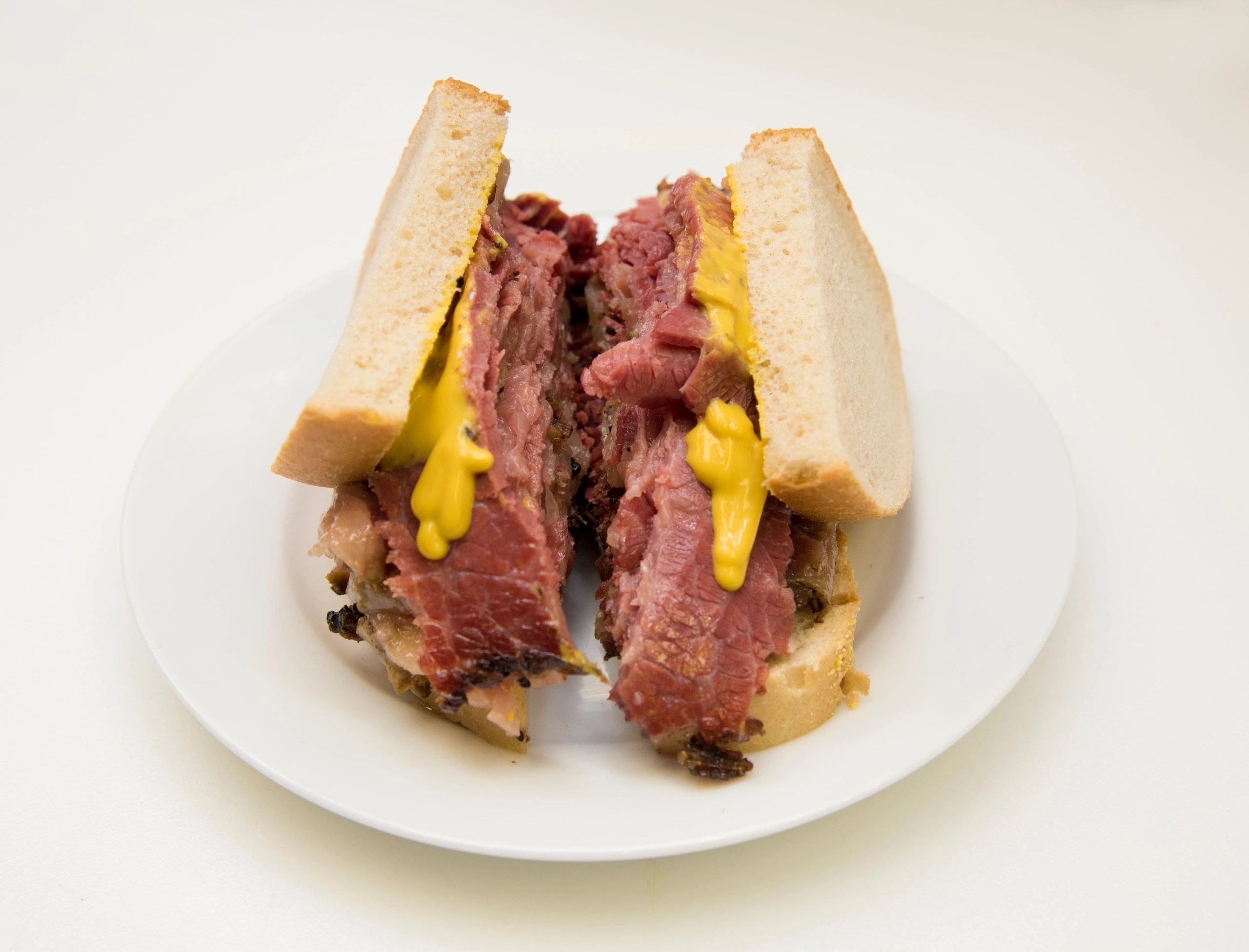 A tall Montreal-style smoked meat sandwich on rye bread with yellow mustard at SumiLicious Smoked Meat & Deli.