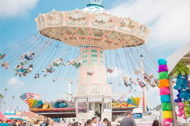 Brightly lit Ferris wheel and midway rides against an evening sky at a summer fair